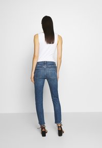 Vaqueros de mezclilla azul ajustados con cintura media, que cuentan con bolsillos traseros y dobladillo deshilachado, combinados con una blusa sin mangas blanca y tacones negros.