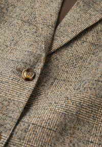 Tissu texturé marron et gris à motif d'une veste, présentant un col cranté, une fermeture à un seul bouton et un motif à carreaux discret.