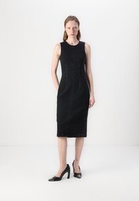Black sleeveless denim dress with a fitted silhouette, side pockets, seams running down the front, and a knee-length hem. Paired with black heels.