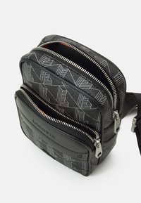 Black fabric bag with geometric pattern, multiple zip compartments, and a textured finish. Features silver hardware and a logo detail.