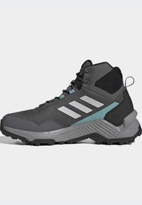 Scarpe da trekking alte grigie realizzate in materiale mesh e sintetico, con tre strisce bianche, accenti turchesi e una suola texture per garantire aderenza.