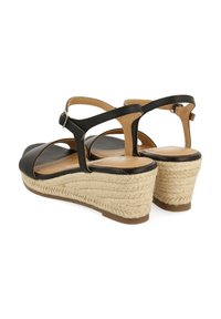Sandalias de cuña negras con tacón de yute trenzado, con un diseño de tira en T y hebilla ajustable en el tobillo. Parte superior de cuero suave con acentos en marrón.