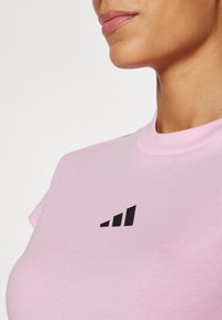 Pink cotton t-shirt features a round neck and short sleeves, with a black geometric logo on the left side of the chest.