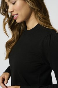 Maglione nero a maglia con scollatura rotonda, polsini a coste e maniche leggermente a sbuffo. Il tessuto ha una consistenza liscia.