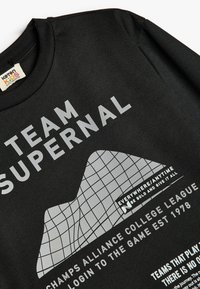 Sort bomulds T-shirt med hvid grafisk tekst og gittermønster. Rund halsudskæring og korte ærmer, med en tekstureret stoffinish.