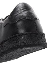 Black leather sneaker with a textured rubber sole, curved seam at the heel, and smooth finish. Features a low-profile design.