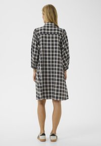 Kék, krémszínű és fekete kockás ruha; térd hosszúságú, testhez simuló felső résszel és puffos ujjakkal. Elöl galléros nyak és gomb részletek találhatók.