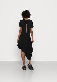 Vestido preto assimétrico com mangas curtas, apresenta um decote nas costas com um fecho de laço e uma bainha fluida e drapeada.