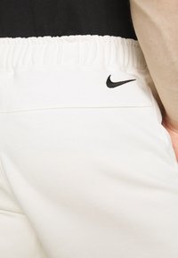 Vita bomulls-joggingbyxor med elastisk midja och en liten svart Nike-logotyp nära fickan, som visar en slät textur och avslappnad design.