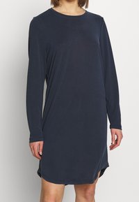 Marineblaues Langarmkleid, weicher Stoff, runder Ausschnitt, lockere Passform, seitliche Schlitze bis zum Oberschenkel, gerader Saum. Geeignet für legere Anlässe.