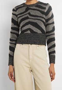 Pull-over rayé noir et métallique avec un col rond et un ourlet côtelé, associé à un pantalon beige à jambes larges. Matière en maille texturée.