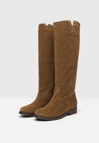 Brązowe zamszowe kozaki do kolan o gładkiej fakturze, zwężonym nosku, bocznym zamku błyskawicznym oraz dekoracyjnymi ćwiekami na górze. Płaska podeszwa i niski obcas.