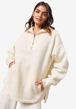 Cremfarbener Fleece-Pullover mit einem halben Reißverschluss-Kragen, großer Fronttasche und gerippten Bündchen. Verfügt über eine weiche, strukturierte Oberfläche.