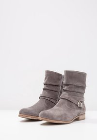Bottes basses en daim gris au design décontracté, avec une fermeture éclair latérale, une sangle décorative à boucle, et une semelle plate imitation bois.