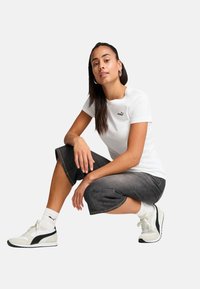 Hvid tætsiddende t-shirt med sort Puma-logo, parret med mørkegrå cropped bukser og hvide sneakers med sorte detaljer. Enkel design, afslappet look.