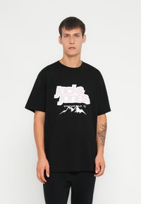 Camiseta de algodón negra con mangas cortas, que presenta un gran logo blanco y rosa y un gráfico de montaña en la parte delantera. Ajuste holgado.