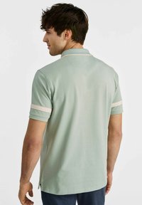 Koszulka polo w jasnym zielonym kolorze z krótkim rękawem i białymi paskami. Posiada klasyczny kołnierzyk oraz boczne rozcięcia zapewniające swobodę ruchów. Materiał z mieszanki bawełny.