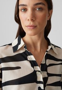Camicia con motivo astratto in bianco e nero, colletto classico, chiusura a bottoni e tessuto liscio, indossata sulla parte superiore del torso di un modello.