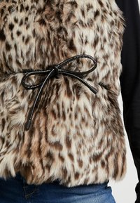 Faux-Fur-Weste in Braun und Creme mit einem Leopardenmuster. Schwarzes Kordelzugdetail in der Taille mit glatter Oberfläche.