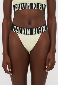 Calvin Klein lavprofil bikini i lys gul med en svart elastisk midje som har logo-tekst. Glatt, elastisk stoff med minimal dekning.