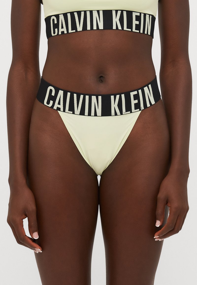 Calvin Klein lavprofil bikini i lys gul med en svart elastisk midje som har logo-tekst. Glatt, elastisk stoff med minimal dekning.