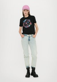 Svart T-skjorte med blomstertrykk og tekst, lyseblå jeans og svarte militærstøvler; rosa caps fullfører antrekket.