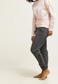 Sudadera rosa claro con "NY PARK" en letras blancas, combinada con pantalones de chándal gris oscuro que presentan "PARK" impreso en el lateral.