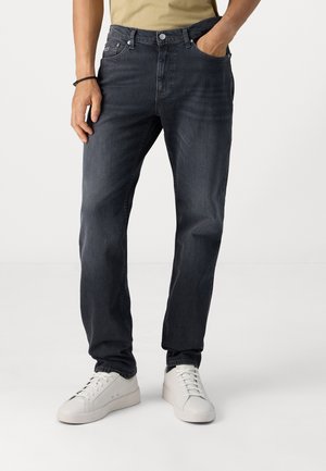 Vaqueros de mezclilla oscura con corte recto, cinco bolsillos y cierre de botón. Combinados con zapatillas blancas. Diseño casual, tejido texturizado.