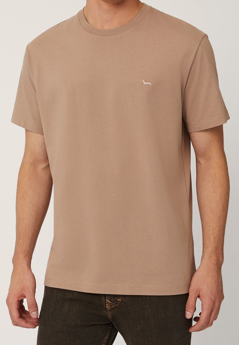 Tan bomullströja med rund hals och korta ärmar. Har en liten broderad tax-logotyp på vänster bröst. Minimalistisk design.