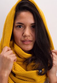 Yellow knit scarf with a textured pattern, draped over the head and neck. Notable tag with contrasting color detail.