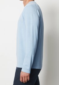 Maglione azzurro chiaro a maniche lunghe con collo rotondo, polsini a coste, texture liscia e silhouette attillata, abbinato a pantaloni scuri.