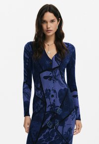 Sügavsinine kootud kleit lillemustriga; pikad varrukad, V-kaelus, istuv siluett ja vertikaalne soonik. Ees on viis musta nööpi.