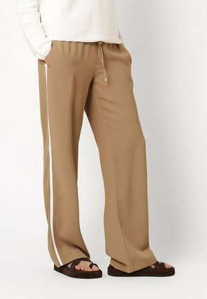 Beige wide-leg pants with white side stripe, elastic drawstring waist, worn with dark brown sandals and white long-sleeve top.