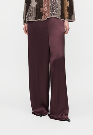 Spodnie z szerokimi nogawkami z satyny w głębokim burgundzie, noszone z wielokolorowym swetrem dzianinowym i czarnymi spiczastymi butami, pokazane od talii do stóp.