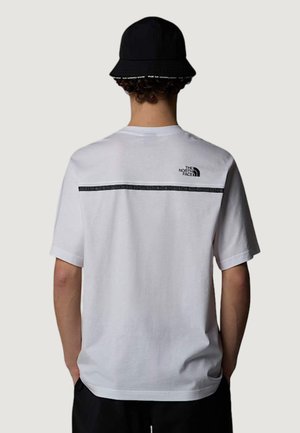 Persona che indossa una maglietta bianca The North Face con logo nero e striscia sulla parte superiore della schiena e un cappello a secchiello nero, vista di spalle.