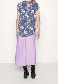 Kortärmad topp i blått med blommönster, kombinerad med en lång lavendelfärgad kjol. Svarta knähöga stövlar fulländar outfiten.