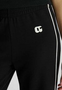 Zwarte trainingsbroek van zachte stof met witte zijkanten en een geborduurd logo op de linkerdij. Elastische tailleband verhoogt het comfort.