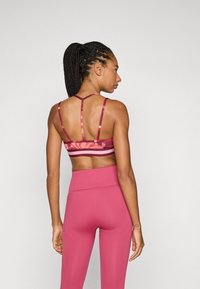 Sportski crop top u ružičastoj boji s cvjetnim uzorkom i tankim trakama, uparen s visokim tajicama u odgovarajućoj ružičastoj tkanini.