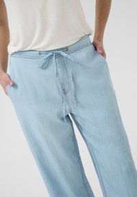 Pantaloni in chambray azzurro chiaro con vita regolabile, tasche laterali e vestibilità morbida. Presentano cuciture a contrasto lungo le cuciture per un tocco di dettaglio.