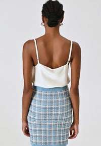 Weißes Satin-Camisole mit dünnen Trägern, kombiniert mit einem figurbetonten blauen Tweed-Rock mit Karomuster und geripptem Bund.