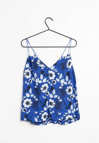 Blue floral cami top featuring thin spaghetti straps, a V-neckline, and a print of white and black flowers with green leaves.