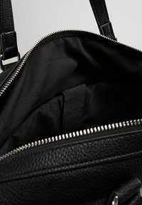 Černá kožená kabelka s texturovaným povrchem, zapínáním na zip a hladkým látkovým vnitřkem s vnitřním páskem.