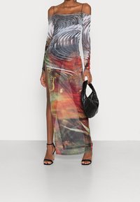 Robe longue et transparente avec un imprimé multicolore abstrait, décolleté épaule, fente haute et manches longues. Sac à main noir matelassé et sandales à talons.