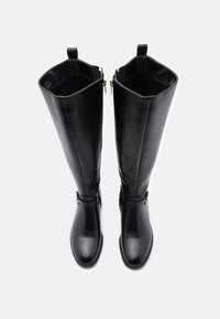 Juodos iki kelių siekiančios bootai, pagaminti iš lygaus odos, su tiesiu šonu, dviem šoninėmis užtrauktukais ir mažą dekoratyvinę sagtimi ant kulkšnies.