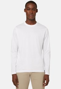 Pitkähihaisen valkoisen T-paidan, joka on valmistettu puuvillasta, pyöreä kaula-aukko ja suora helma. Suojaava pinta, jossa ei ole näkyviä kuvioita tai grafiikoita.