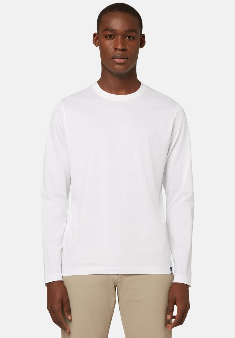 Pitkähihaisen valkoisen T-paidan, joka on valmistettu puuvillasta, pyöreä kaula-aukko ja suora helma. Suojaava pinta, jossa ei ole näkyviä kuvioita tai grafiikoita.