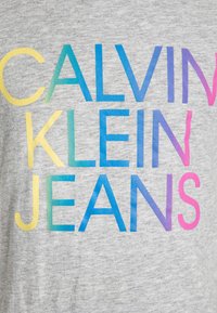 Szary t-shirt z odważnym, gradientowym napisem w kolorach żółtym, niebieskim, fioletowym i różowym, tworzącym tekst "CALVIN KLEIN JEANS". Materiał z mieszanki bawełny.