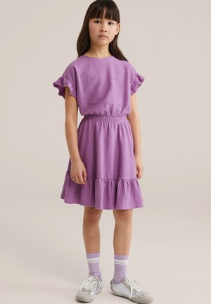 Vijolična obleka s kratkimi nagubanim rokavi in elastičnim pasom, s krilom, ki se razširi. Oblečena s sivimi supergami in vijoličnimi nogavicami s črtami.