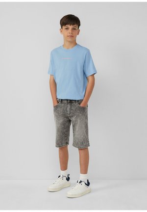 Lichtblauw T-shirt met korte mouwen en roze tekst, gecombineerd met grijze denim shorts, witte sneakers met marineblauwe accenten en witte crew-sokken.