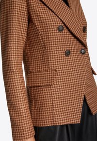 Ruskea koiranhampuu-kuvioinen bleiseri, jossa on kaksirivinen etuosa, mustat napit ja kylkikoju, sekä muotoiltu istuvuus ja teksturoitu kangas.